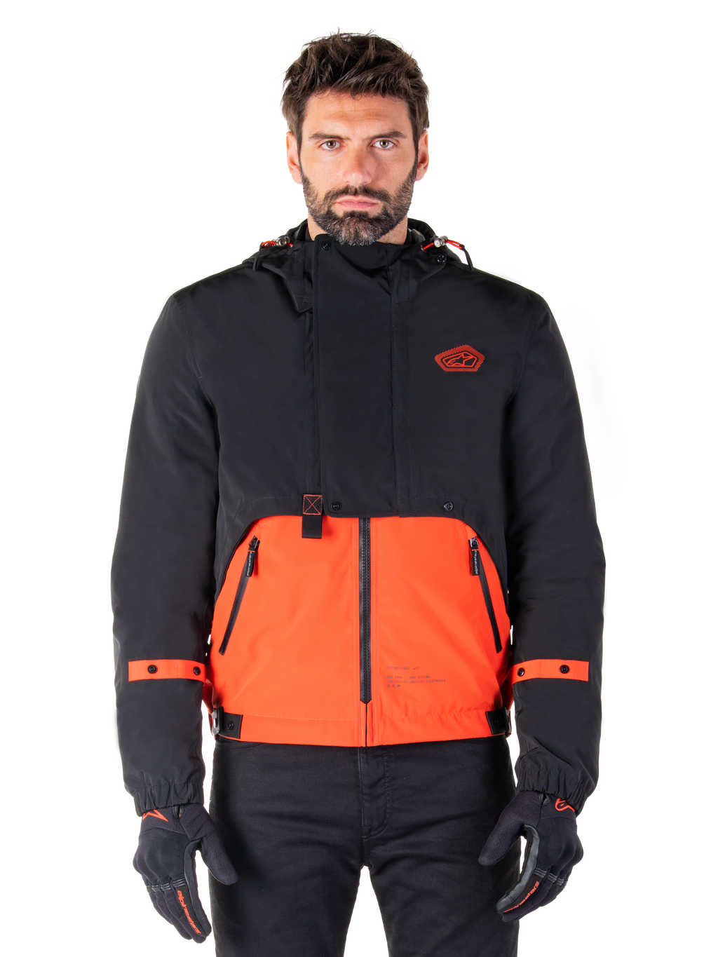 Alpinestars Mootant Waterproof Parka, veste de moto modulaire en Spicy Orange et noir, portée par un mannequin avec des gants assortis, présente un design à capuche avec des empiècements bicolores, une fermeture éclair frontale et des poignets réglables, vêtement de moto urbain contemporain
