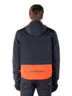 Parka imperméable Alpinestars Mootant en Spicy Orange et noir, vue arrière montrant la partie supérieure noire avec capuche et le panneau inférieur orange arborant le logo MO.ST.EQ., vêtement de moto streetwear fonctionnel
