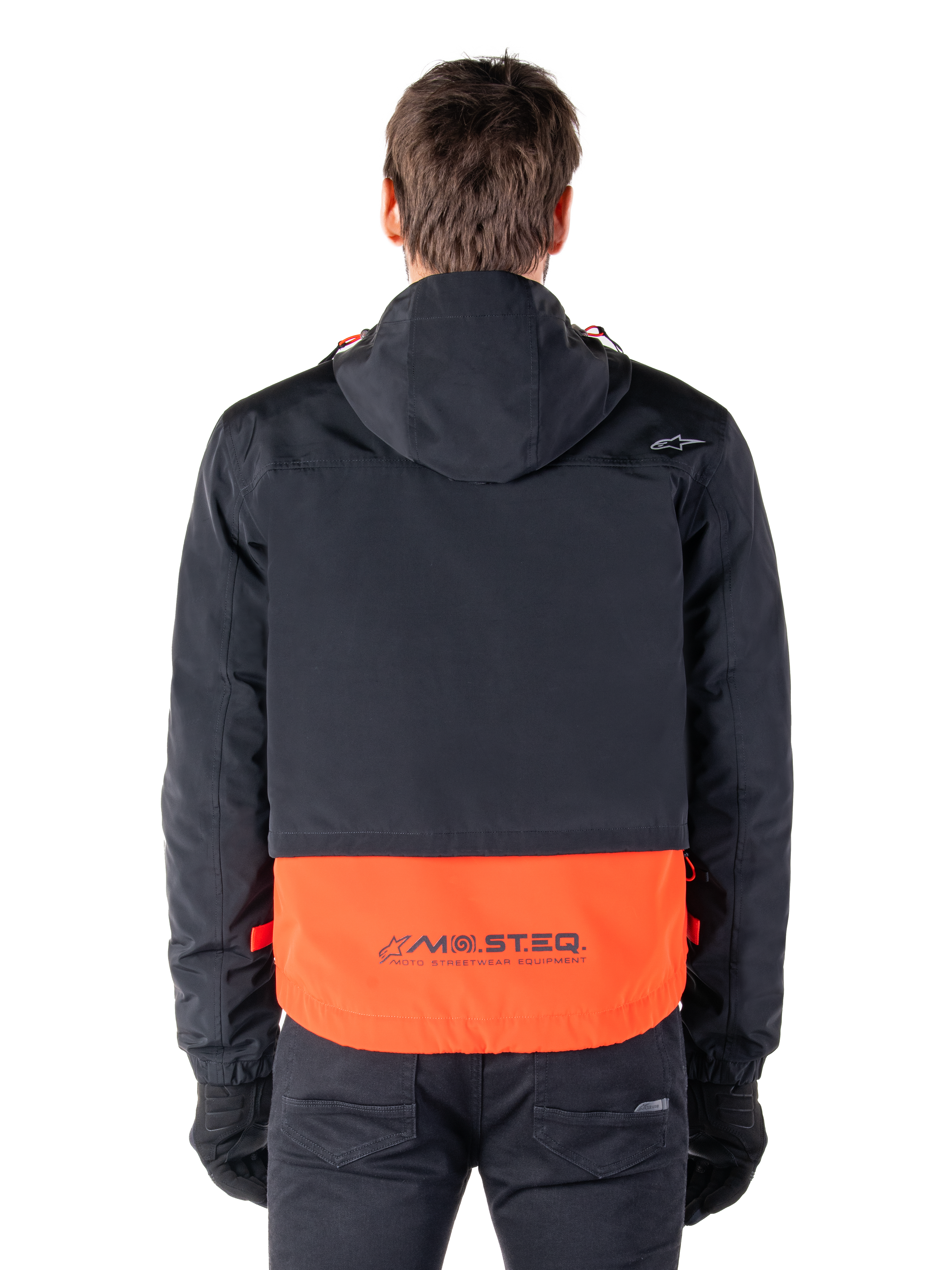 Parka imperméable Alpinestars Mootant en Spicy Orange et noir, vue arrière montrant la partie supérieure noire avec capuche et le panneau inférieur orange arborant le logo MO.ST.EQ., vêtement de moto streetwear fonctionnel
