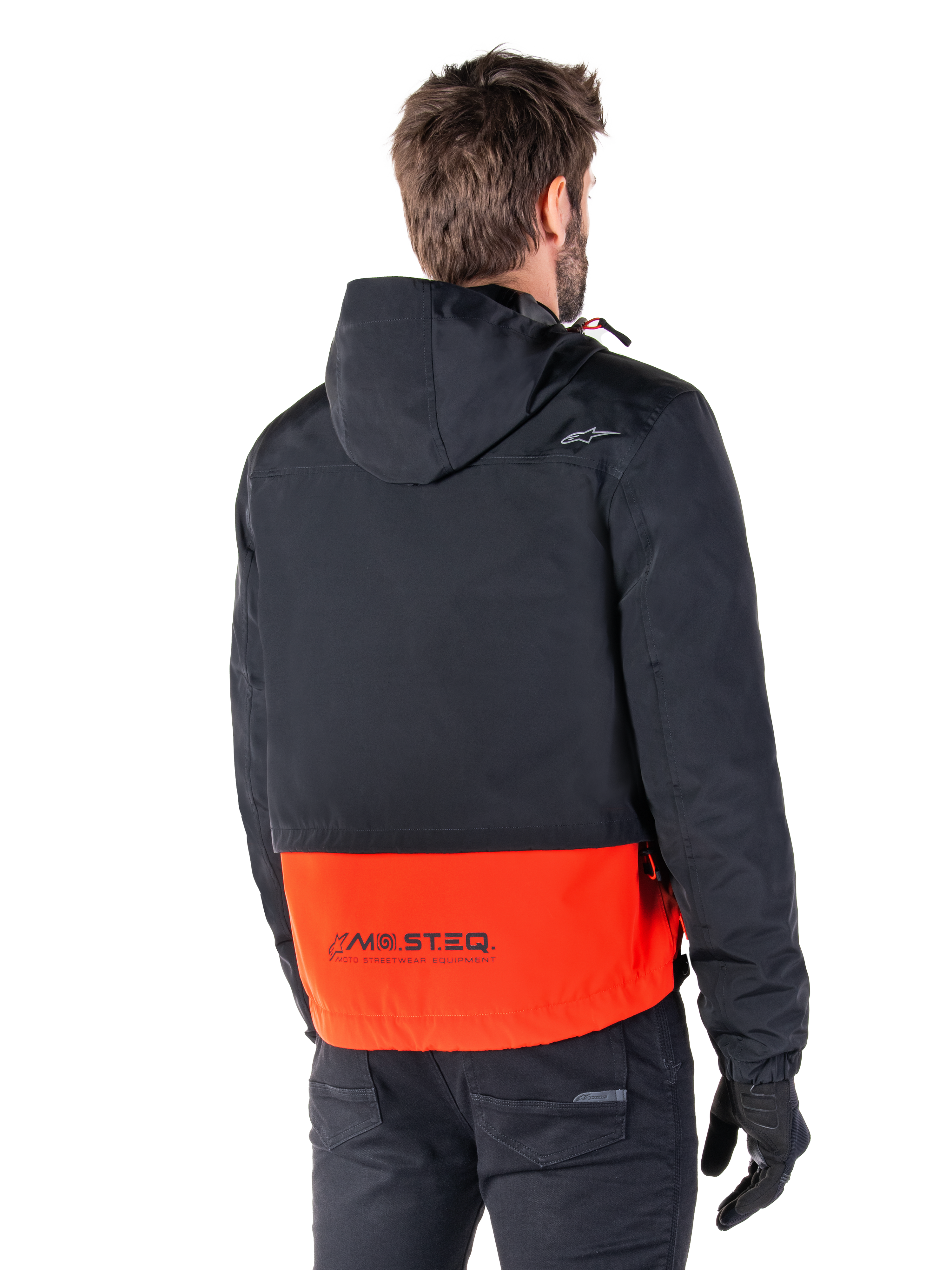 Parka imperméable Alpinestars Mootant, orange épicé et noir, vue arrière sur un mannequin homme, dotée d'une partie supérieure noire à capuche et d'une partie inférieure orange vif avec le logo MO.ST.EQ., veste de moto urbaine contemporaine portée avec un pantalon et des gants noirs