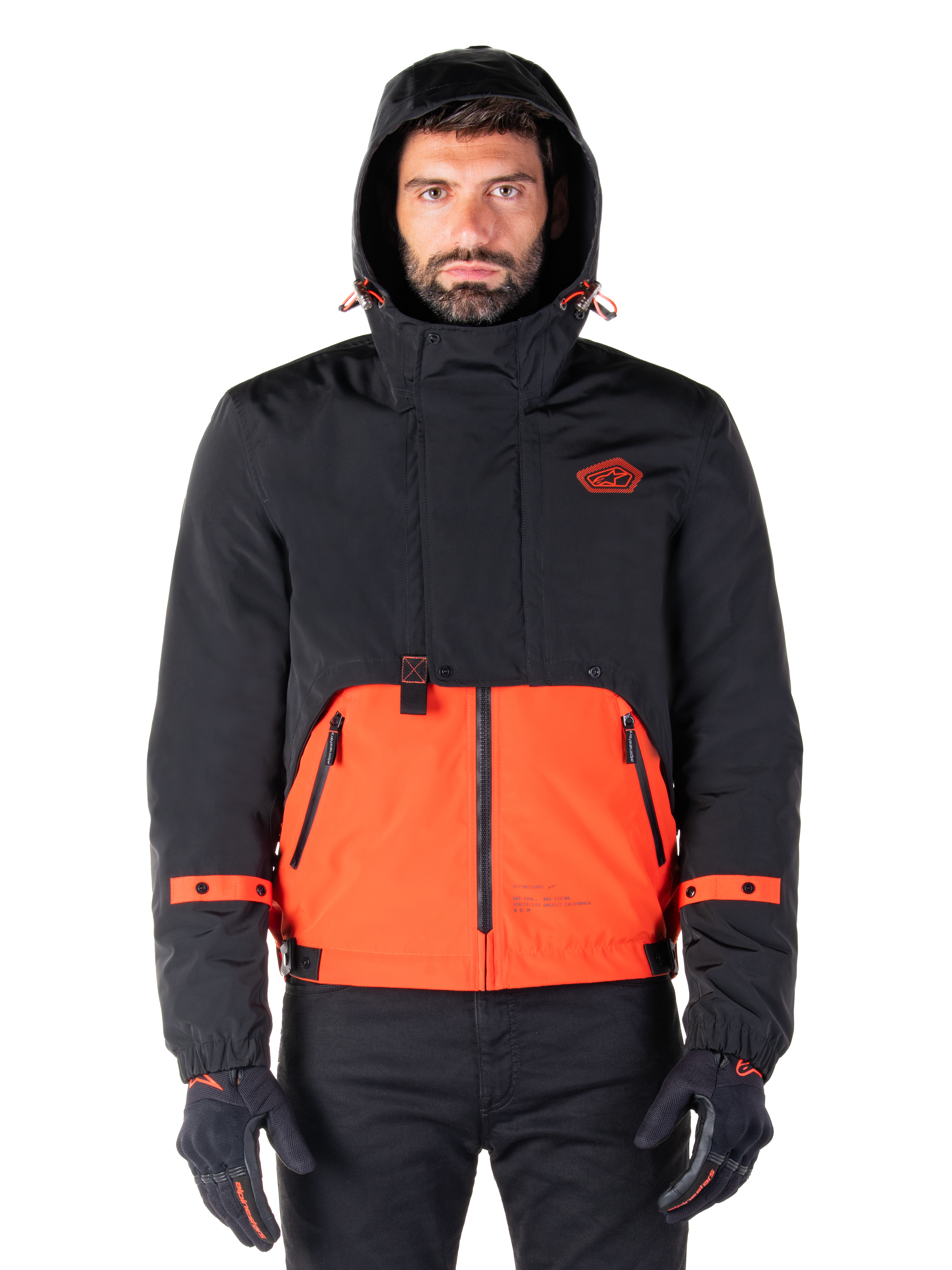 Alpinestars Mootant Waterproof Parka, veste de moto, orange épicé et noir, design modulaire toutes saisons avec capuche, poches avant zippées et détails de sangles orange sur les manches, portée par un mannequin avec des gants et un pantalon noirs
