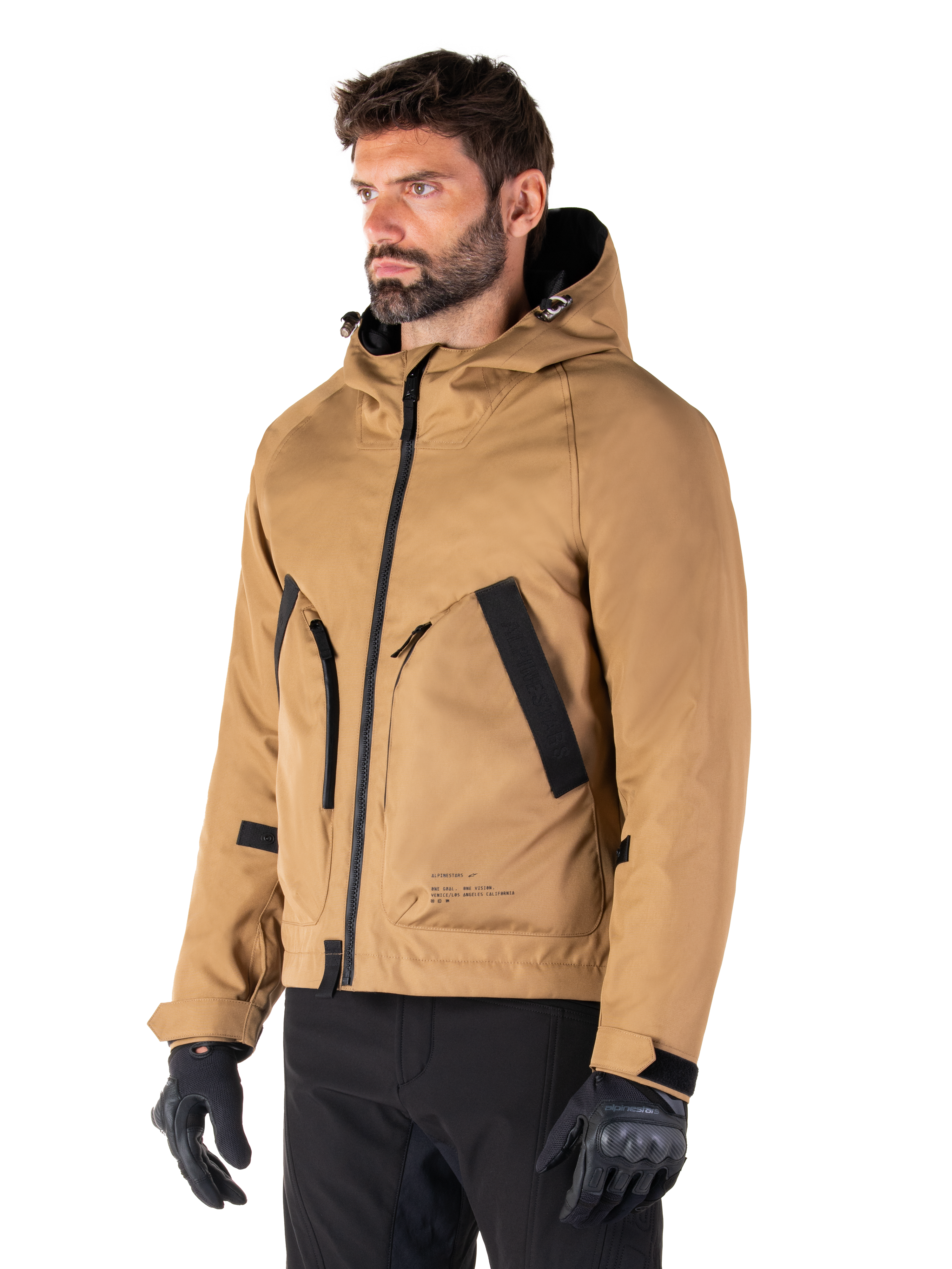 Alpinestars Morush Waterproof Parka, Utility Brown, mannelijk model draagt parka met zwarte motorhandschoenen en zwarte broek, minimalistisch op streetwear geïnspireerd ontwerp met een stormbestendige capuchon en grote voorzakken, waterdichte motorkleding
