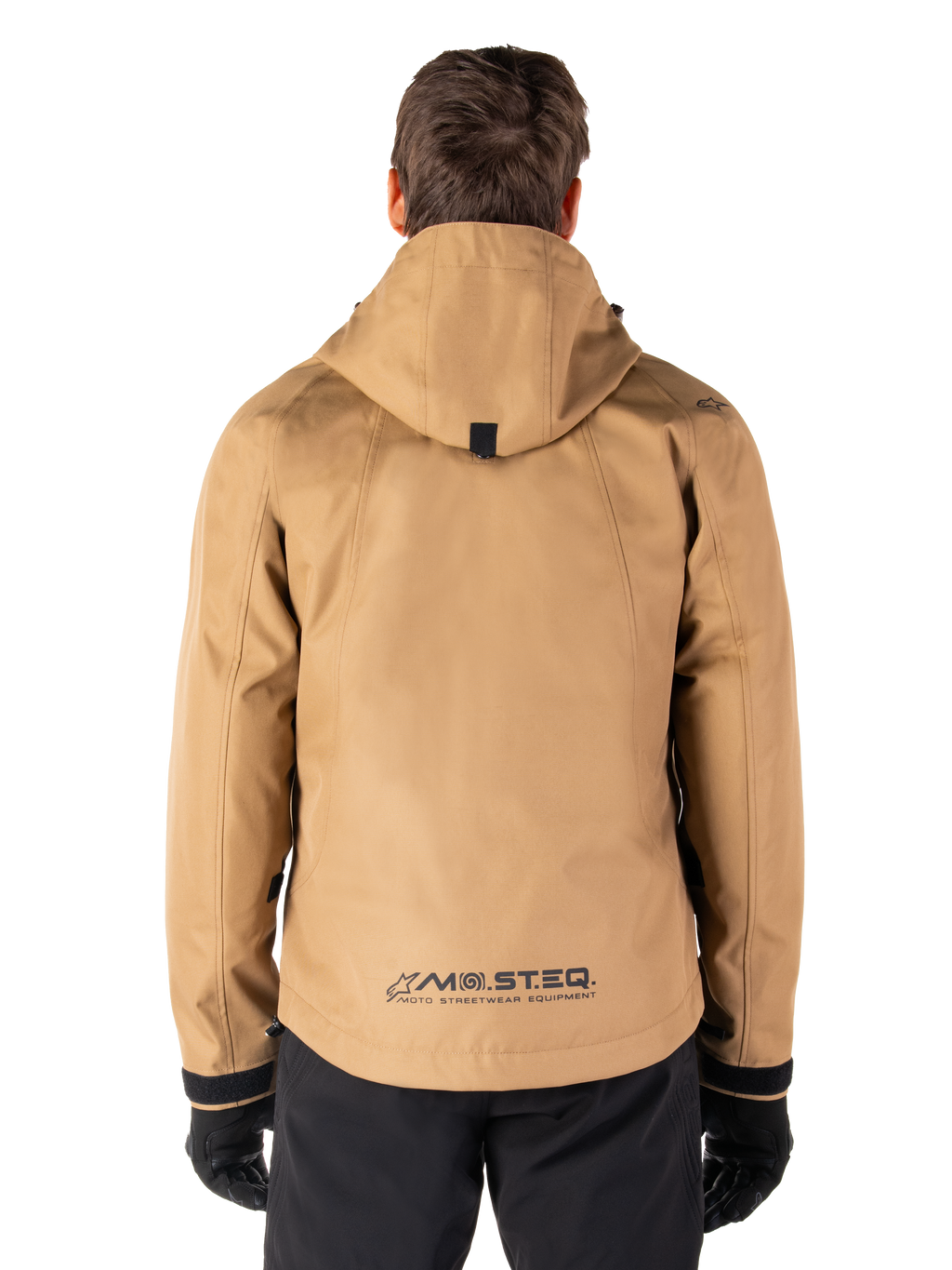 Alpinestars Morush Waterproof Parka, Utility Brown, achteraanzicht, voorzien van een capuchon en MO.ST.EQ.-branding op de onderrug, gecombineerd met een zwarte broek en handschoenen, moderne op streetwear geïnspireerde motorkleding