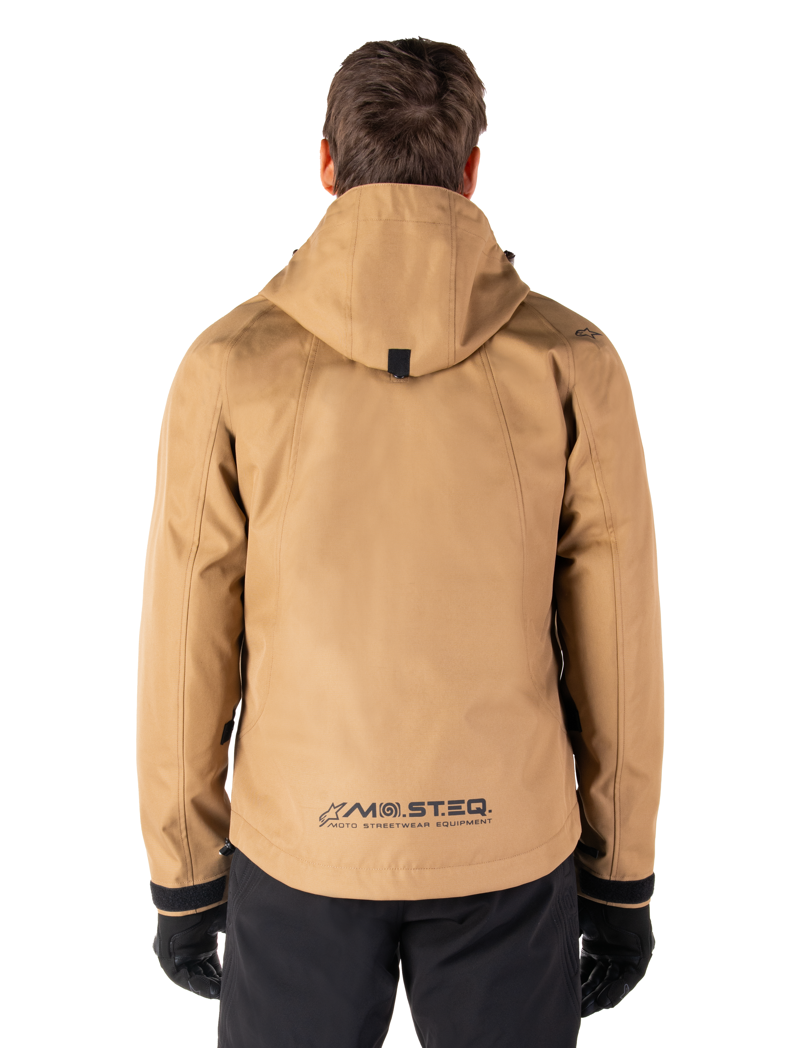 Alpinestars Morush Waterproof Parka, Utility Brown, achteraanzicht, voorzien van een capuchon en MO.ST.EQ.-branding op de onderrug, gecombineerd met een zwarte broek en handschoenen, moderne op streetwear geïnspireerde motorkleding