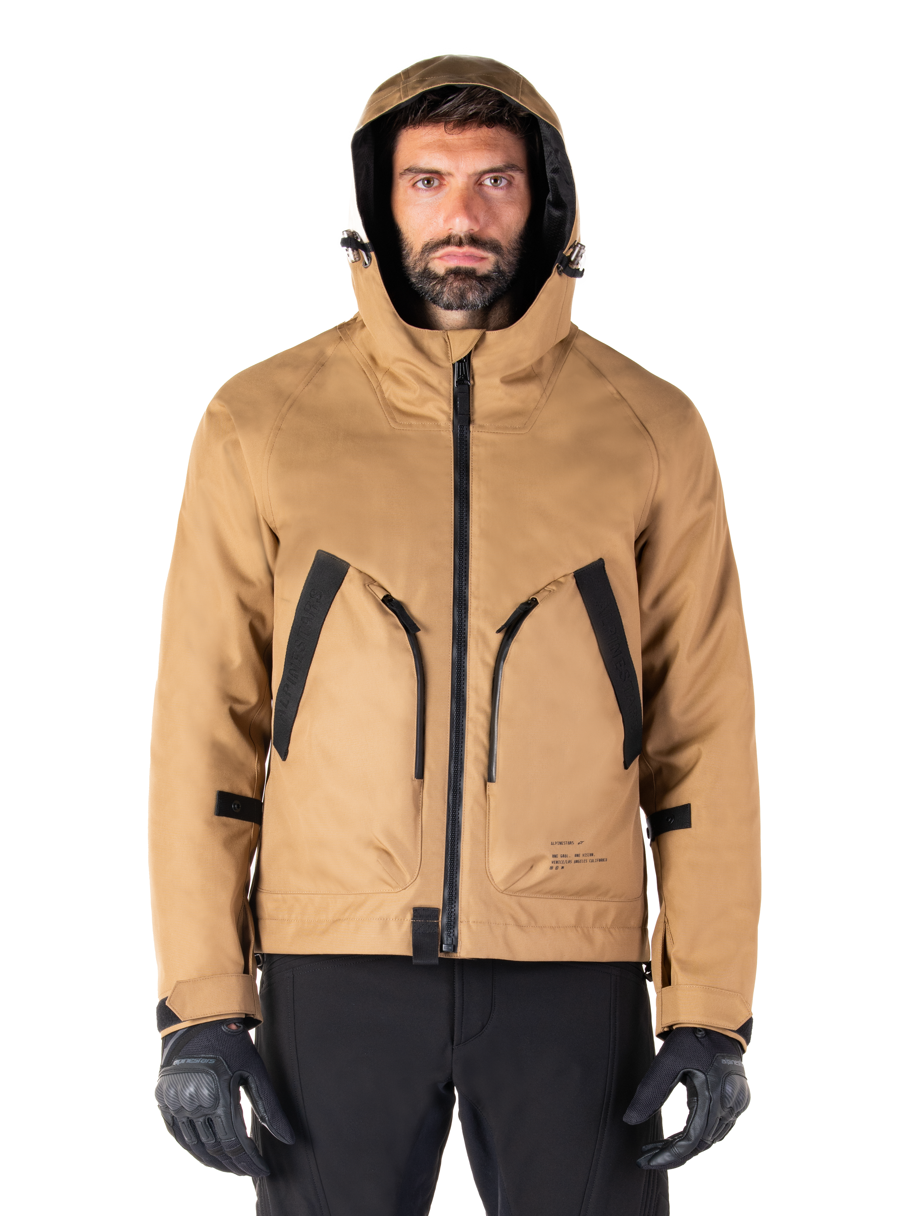 Alpinestars Morush Waterproof Parka, motorjas, Utility Brown, streetwear-geïnspireerd ontwerp met capuchon en grote voorzakken met zwarte accenten, gedragen met zwarte motorhandschoenen en broek, urban contemporary motorkleding