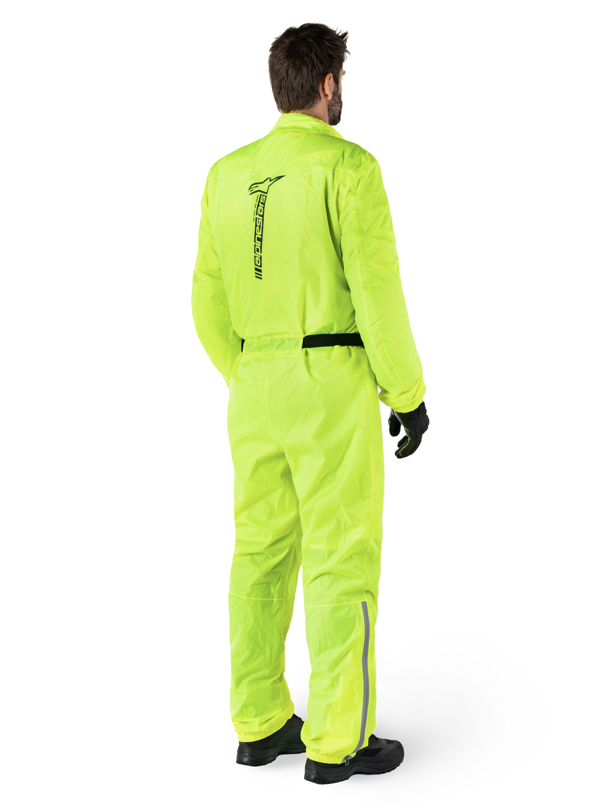 Combinaison Alpinestars Hurricane Rain V2, Jaune Fluo, vue arrière d'un motard portant une combinaison de pluie de moto une pièce, avec un logo Alpinestars noir au dos, une ceinture noire et des bandes réfléchissantes sur le bas des jambes, portée avec des gants et des bottes noirs
