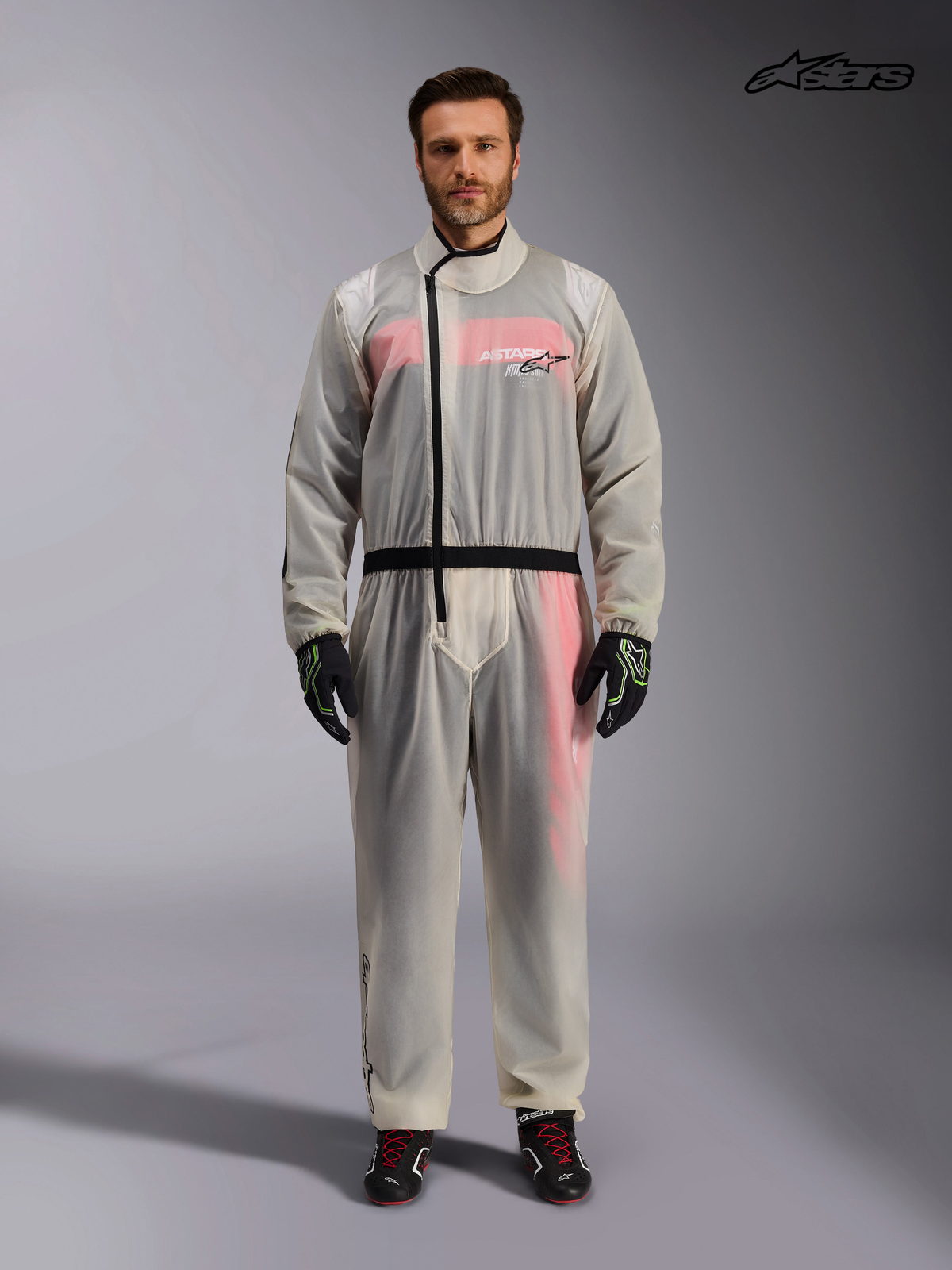 Combinaison Imperméable Kart d'Alpinestars, combinaison de karting transparente pour homme en couleur claire, vue de face sur un modèle montrant la fermeture à glissière asymétrique et la taille élastiquée