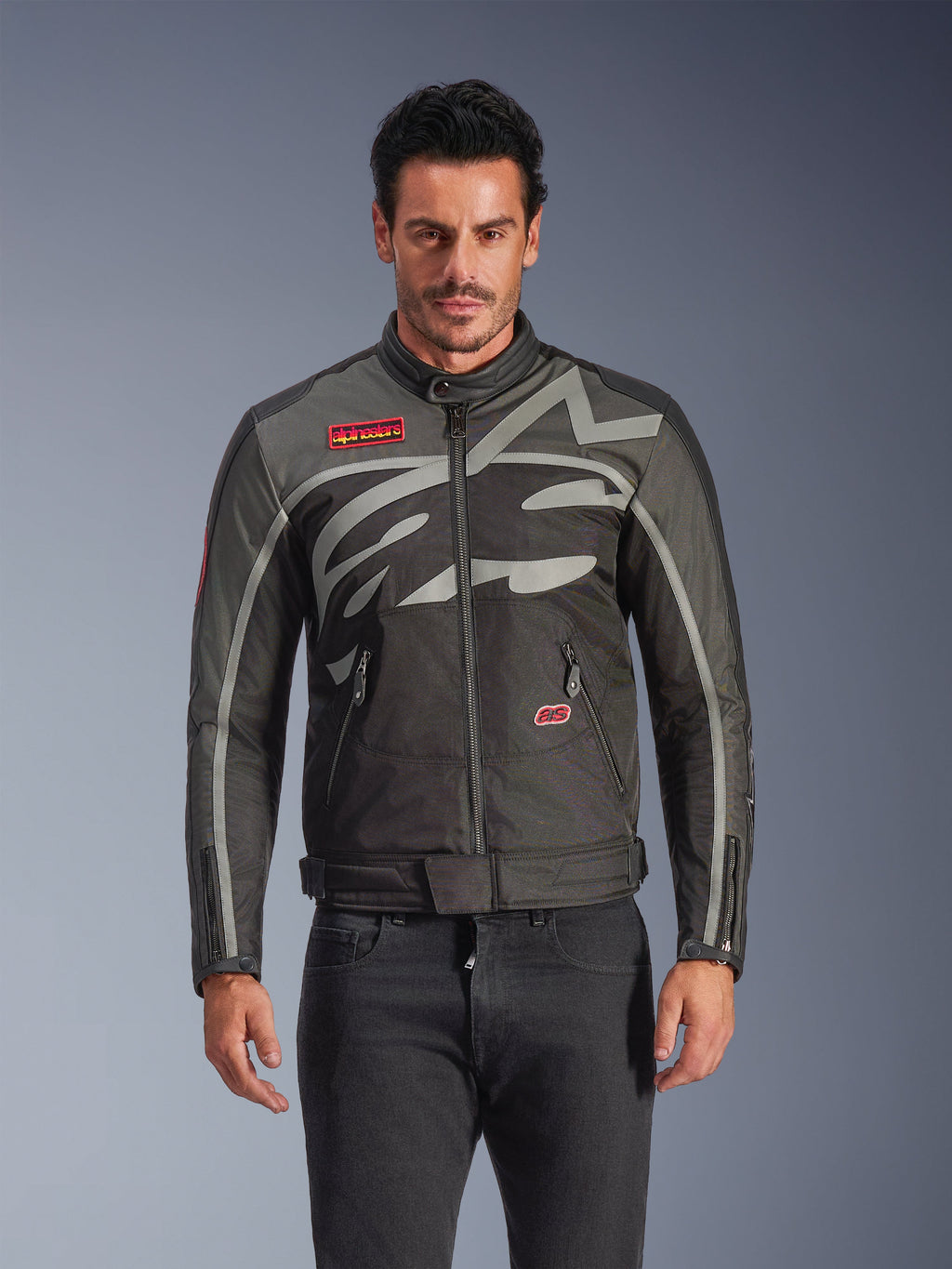 Veste Alpinestars Axton, veste de moto urbaine pour homme, noir et anthracite avec des touches de rouge, dotée d'un large motif graphique gris clair enveloppant, écussons avec logo rouge sur la poitrine et la poche, fermeture éclair frontale et poignets zippés, design de course d'inspiration vintage pour la conduite urbaine