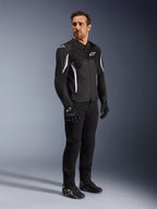 Alpinestars AST V3 Air Jacke, Schwarz mit weißen Akzenten und Branding, leichte Motorradjacke mit Mesh-Belüftung, getragen von einem Mann mit schwarzer Motorradhose, Handschuhen und Schuhen, technische Sommer-Fahrausrüstung für Sport und Straße.