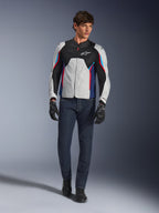 Mannequin homme portant la veste Alpinestars AST V3 Air en Silver Deep Blue Bright Red, dotée d'une ventilation en maille et de panneaux perforés, associée à un jean de moto en denim foncé et des gants noirs, équipement de moto sportif pour temps chaud.