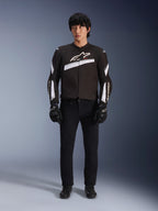 Veste Alpinestars T-GP Plus R V4, noir et blanc, veste de moto en textile sport, portée par un mannequin avec un pantalon et des gants noirs, logo Alpinestars blanc sur la poitrine et les manches, design épuré inspiré de la course