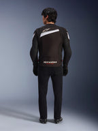 Veste Alpinestars T-GP Plus R V4, veste de moto sport en textile, noir et blanc, vue arrière avec logo Alpinestars blanc et marquage 'RACING AHEAD', portée avec un pantalon et des bottes noirs, design profilé pour la conduite de performance.