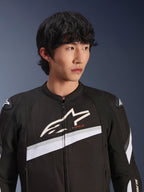 Veste Alpinestars T-GP Plus R V4, noir et blanc, veste de moto en textile portée par un mannequin homme, avec un grand logo étoile blanc sur la poitrine, des bandes diagonales blanches et des protections d'épaules DFS Lite, équipement de route d'inspiration sportive.