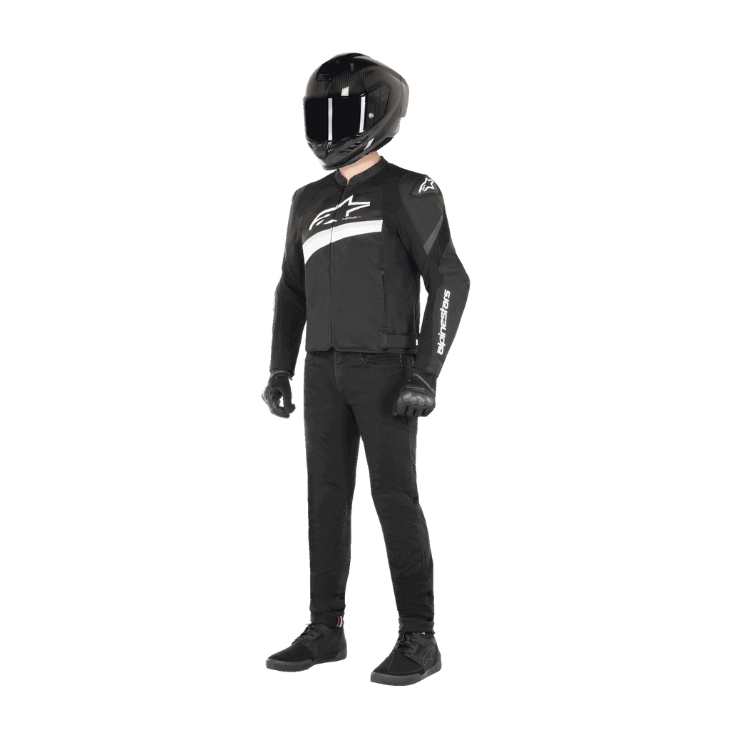 Pilote portant la veste Alpinestars T-GP Plus R V4 Airflow Noir et Blanc, veste de moto en textile avec panneaux en mesh et logo Alpinestars blanc, associée à un casque noir, des gants de pilotage noirs, un pantalon noir et des chaussures noires.