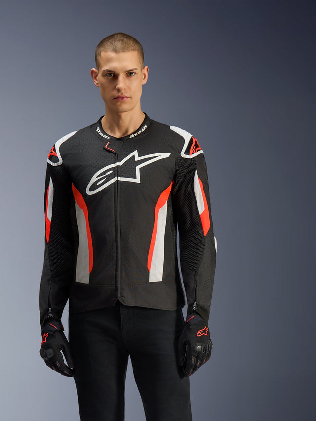 Mannequin homme portant la veste Alpinestars T-GP Air, noir avec accents rouge fluo et blancs, grand logo Alpinestars sur la poitrine, avec panneaux perforés au laser et protections aux épaules, gants de moto noirs, équipement de moto coupe sport pour temps chaud