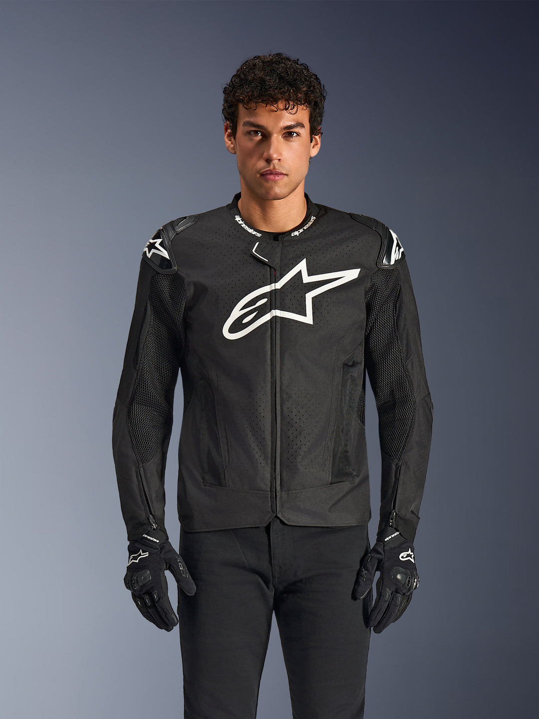 Alpinestars T-GP Air Jacket, veste de moto perforée noire avec logo blanc, portée avec gants noirs, design sportif texturé pour ventilation, protection aux épaules