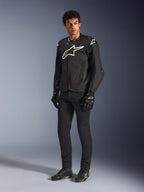 Blouson Alpinestars T-GP Air, veste de moto en textile noir, porté par un mannequin avec pantalon et gants noirs assortis, arborant un logo Alpinestars blanc sur la poitrine et les épaules, des panneaux en maille ventilés et une coupe sportive dérivée de la course