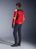 Alpinestars T-GP Air Jacke, Rückansicht eines Mannes in einer leuchtend roten und neongroten Textiljacke mit schwarzen Mesh-Einsätzen und weißen Protektoren-Schleifern, kombiniert mit dunkelblauen Jeans und schwarzen Motorradschuhen, Sport-Motorradausrüstung.