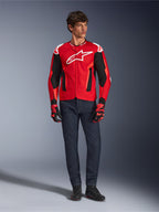 Alpinestars T-GP Air Jacke, Hellrot Fluo-Rot Schwarz, männliches Model in kompletter Motorradausrüstung mit dunkelblauer Jeans und passenden Handschuhen, Sport-Textiljacke mit perforierten Mesh-Einsätzen und weißem Astars-Logo, Studioaufnahme.