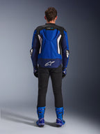 Blouson Alpinestars T-GP Air, Bleu Brillant Marine Blanc, vue de dos montrant la bosse aérodynamique et les panneaux de ventilation en maille, logo Alpinestars blanc en bas du dos, porté avec un pantalon noir et des bottes de course bleues