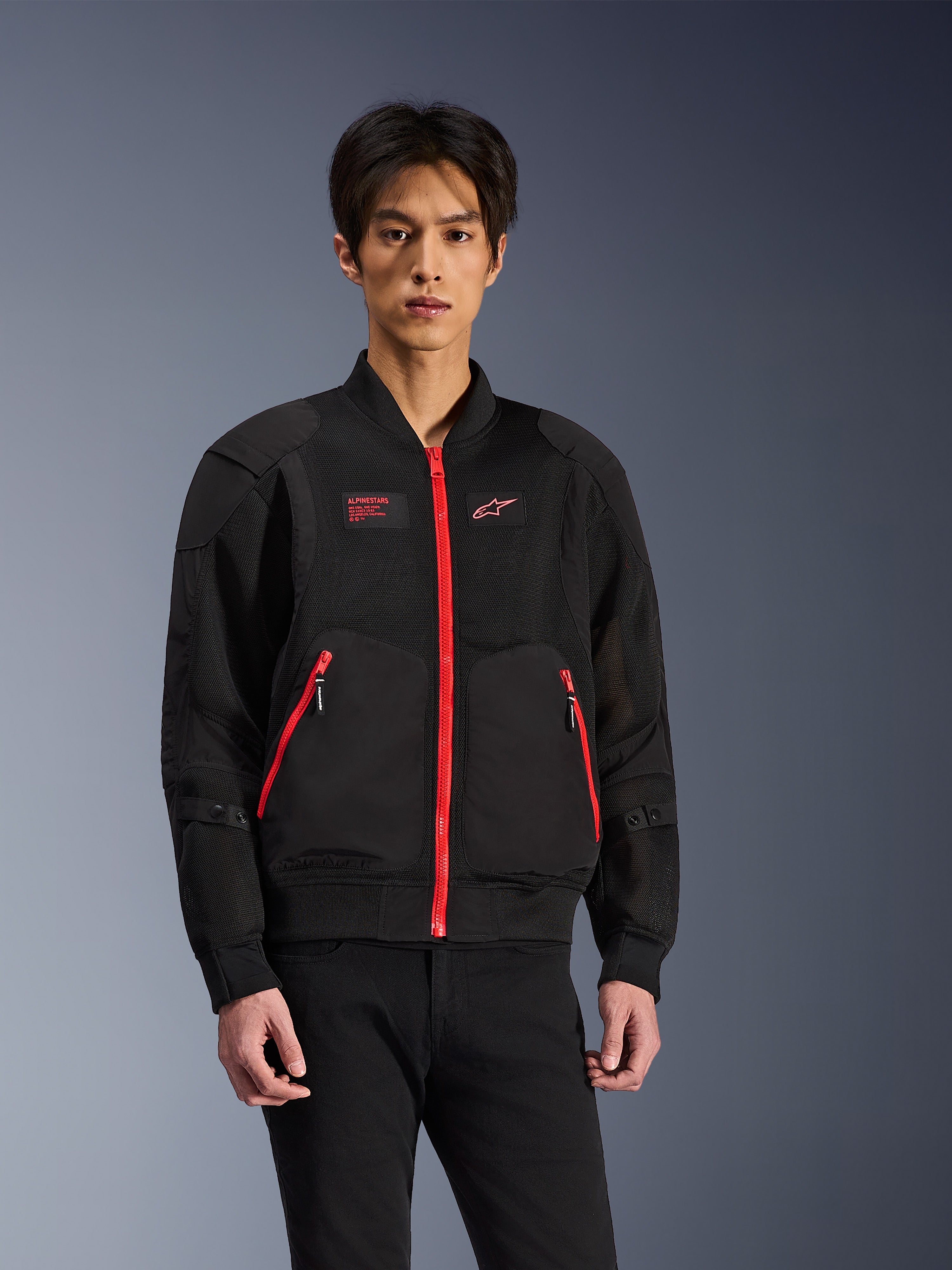Alpinestars Flight Air Jacket en noir et rouge vif, veste de moto urbaine de style bomber portée par un mannequin, avec panneaux de ventilation en maille, fermeture éclair avant rouge, détails de poches rouges et logo sur la poitrine, assortie à un pantalon noir
