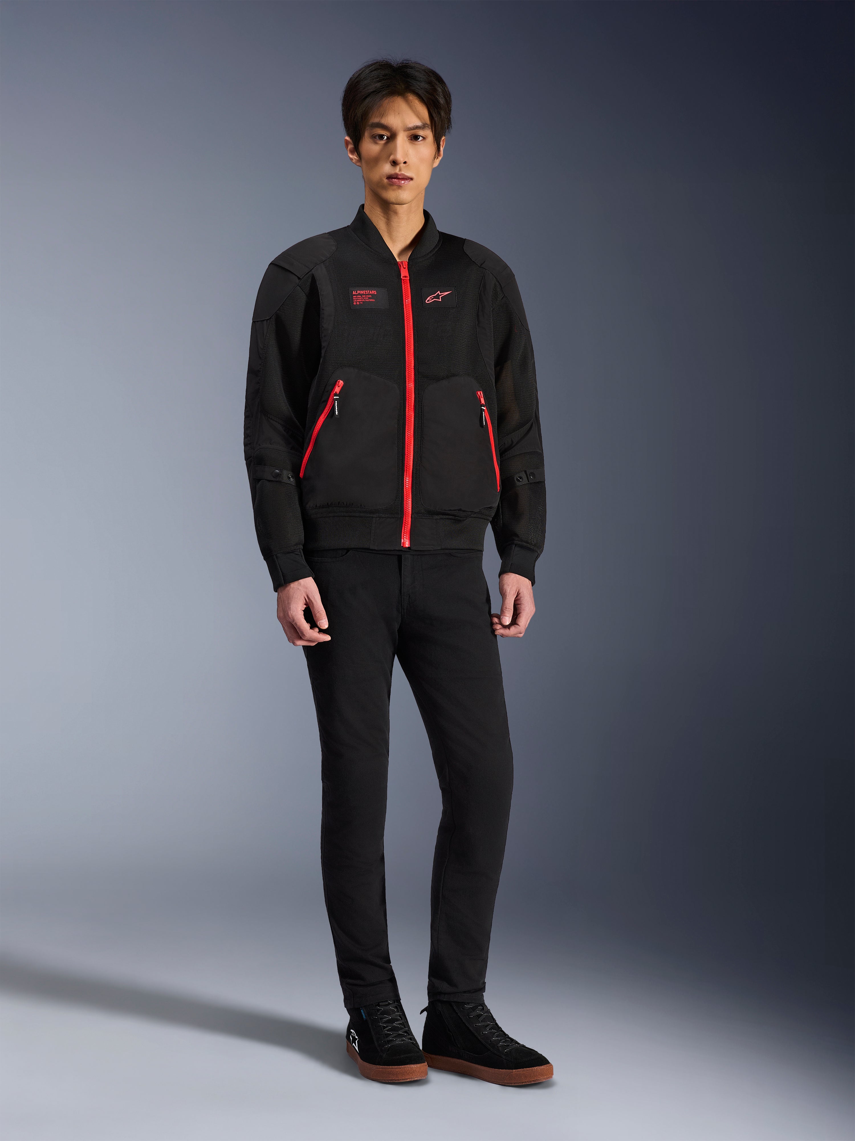 Veste Alpinestars Flight Air en Noir Rouge Vif, veste de moto urbaine de style bomber avec panneaux en maille 3D et fermetures éclair rouge vif, portée par un mannequin avec un pantalon slim noir et des baskets noires, équipement de moto contemporain d'inspiration streetwear