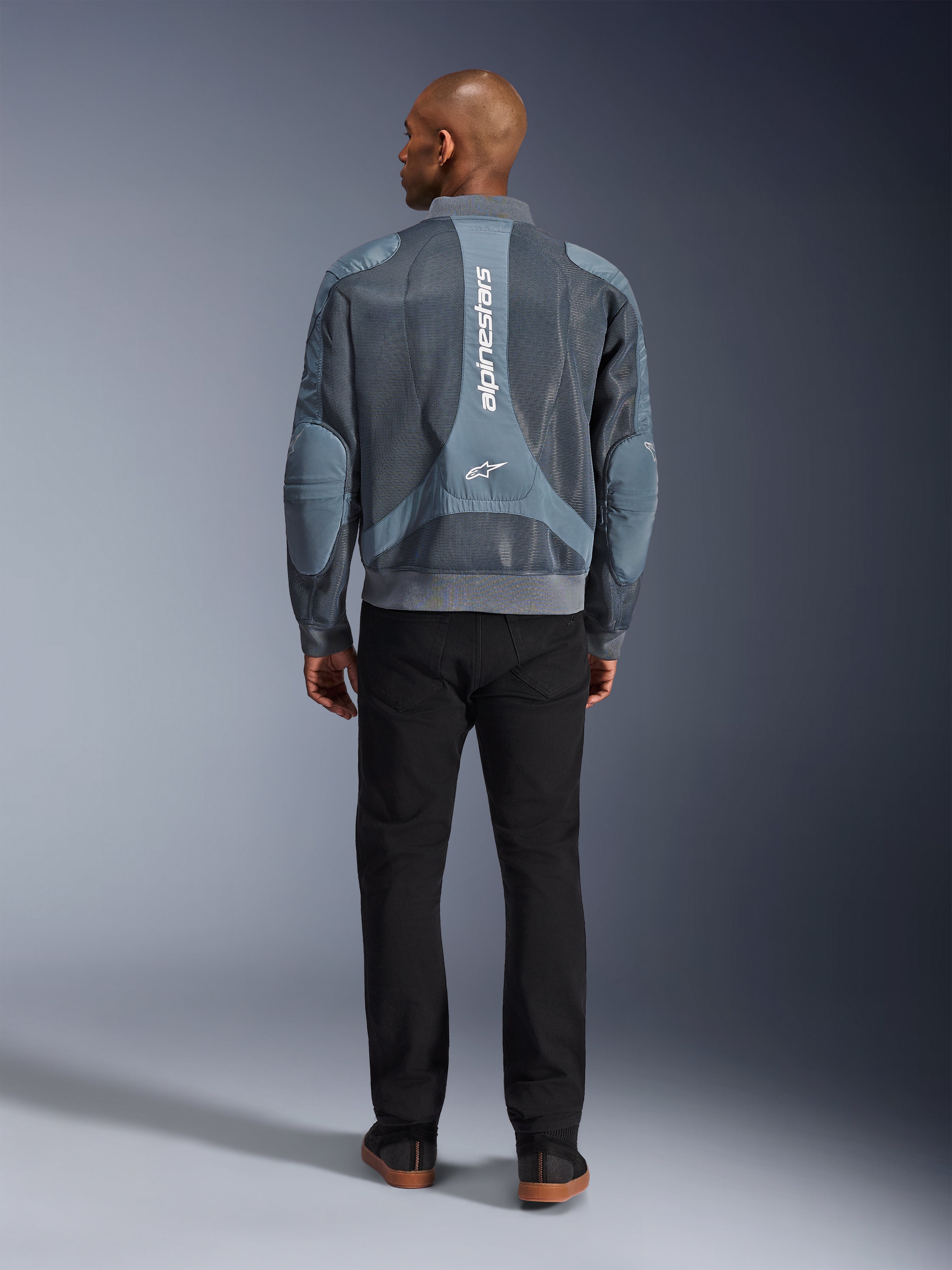 Alpinestars Flight Air Jacke in Storm Gray, Rückansicht eines männlichen Models in einer urbanen Motorradjacke mit 3D-Mesh-Paneelen und vertikalem Alpinestars-Branding, kombiniert mit einer schwarzen Hose für einen modernen Pendler-Look