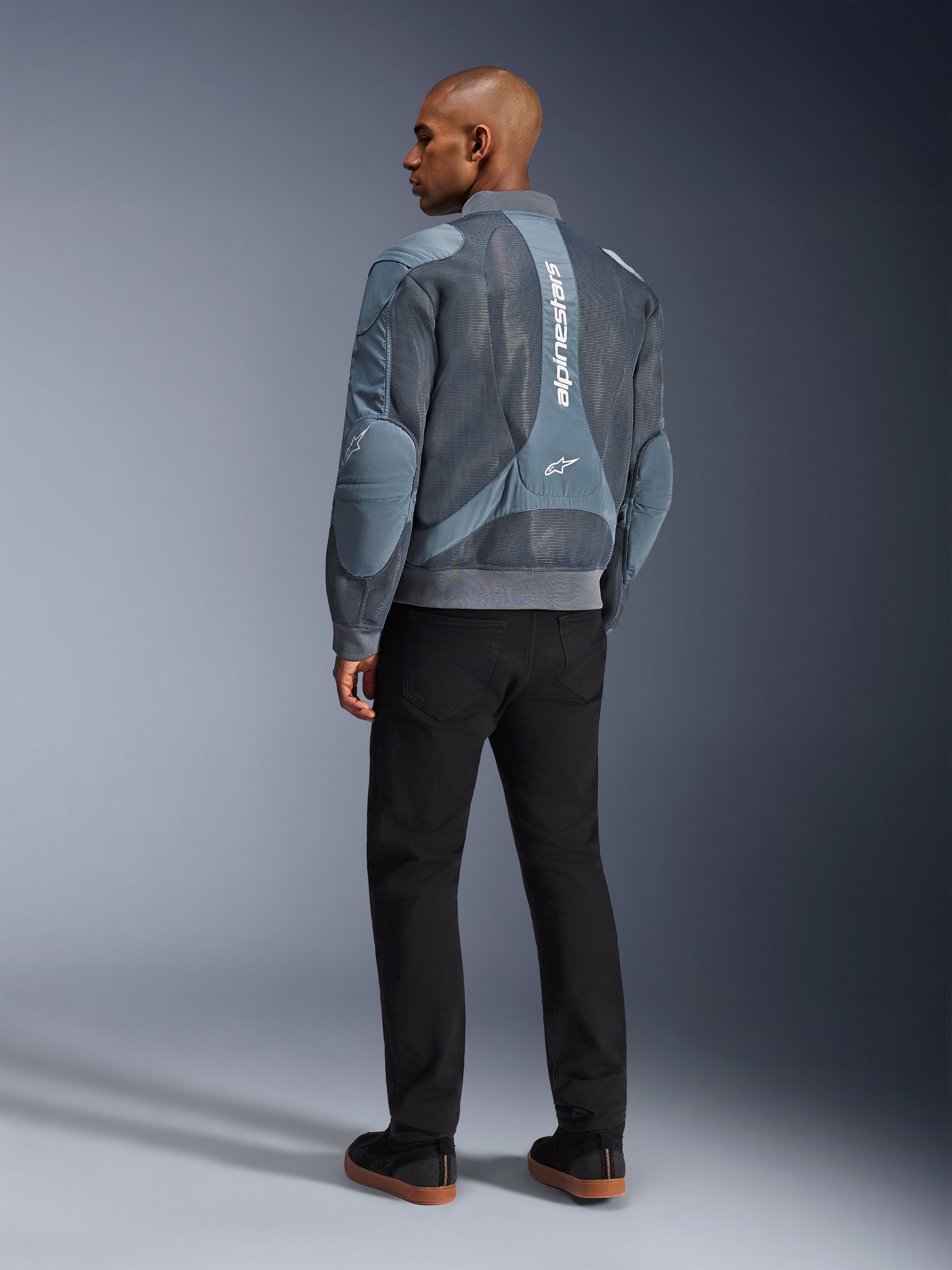 Alpinestars Flight Air Jacke, Motorradjacke in Storm Gray, Rückansicht, mit 3D-Mesh-Belüftungseinsätzen und vertikalem weißem Alpinestars-Branding, getragen mit schwarzer Hose und schwarzen Sneakern, urbaner Pendler-Stil