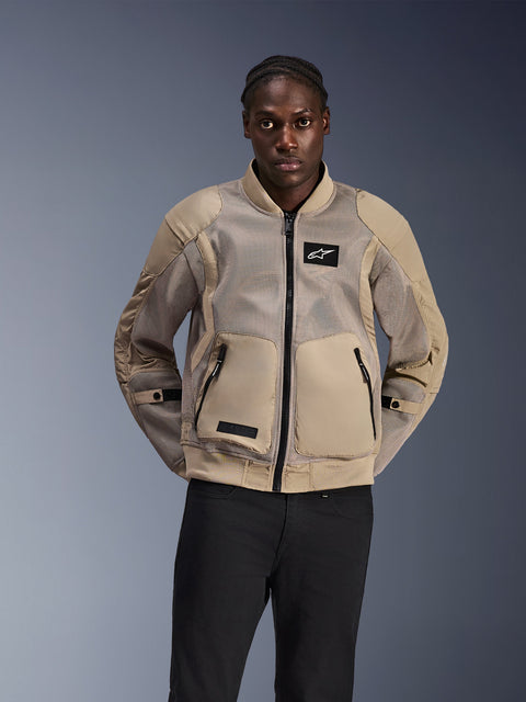 Veste Alpinestars Flight Air, veste de moto urbaine style bomber, beige clair, dotée de larges panneaux en maille 3D pour la ventilation et de grandes poches avant, portée par un homme avec un pantalon noir, design moderne inspiré du sport automobile pour rouler par temps chaud