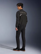 Alpinestars Unite Jacke, Urban-Motorradjacke, Schwarz und Dunkelgrau, Rückansicht mit großem umrandetem Alpinestars-Logo, reflektierende Paspeln und Einsätze, minimalistisches Softshell-Design, getragen mit schwarzer Hose und Freizeitschuhen
