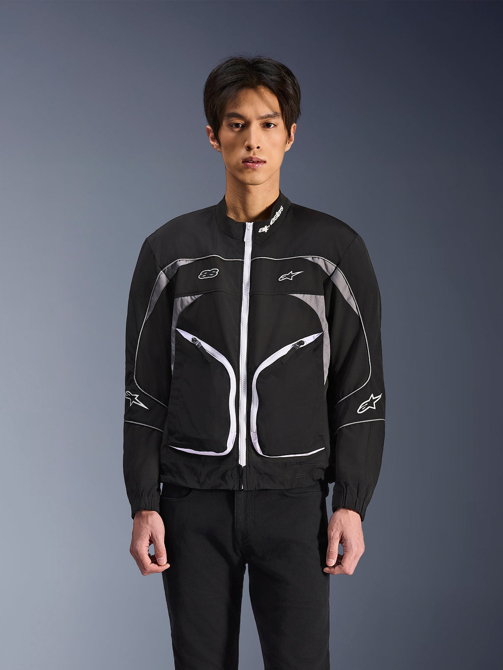 Alpinestars Unite Jacke, minimalistische urbane Motorradjacke, Schwarz und Dunkelgrau mit weißen Akzenten, weißer Frontreißverschluss, reflektierende Paspeln und Alpinestars-Branding auf Brust und Ärmeln, moderner Streetwear-Stil für Motorradfahrer