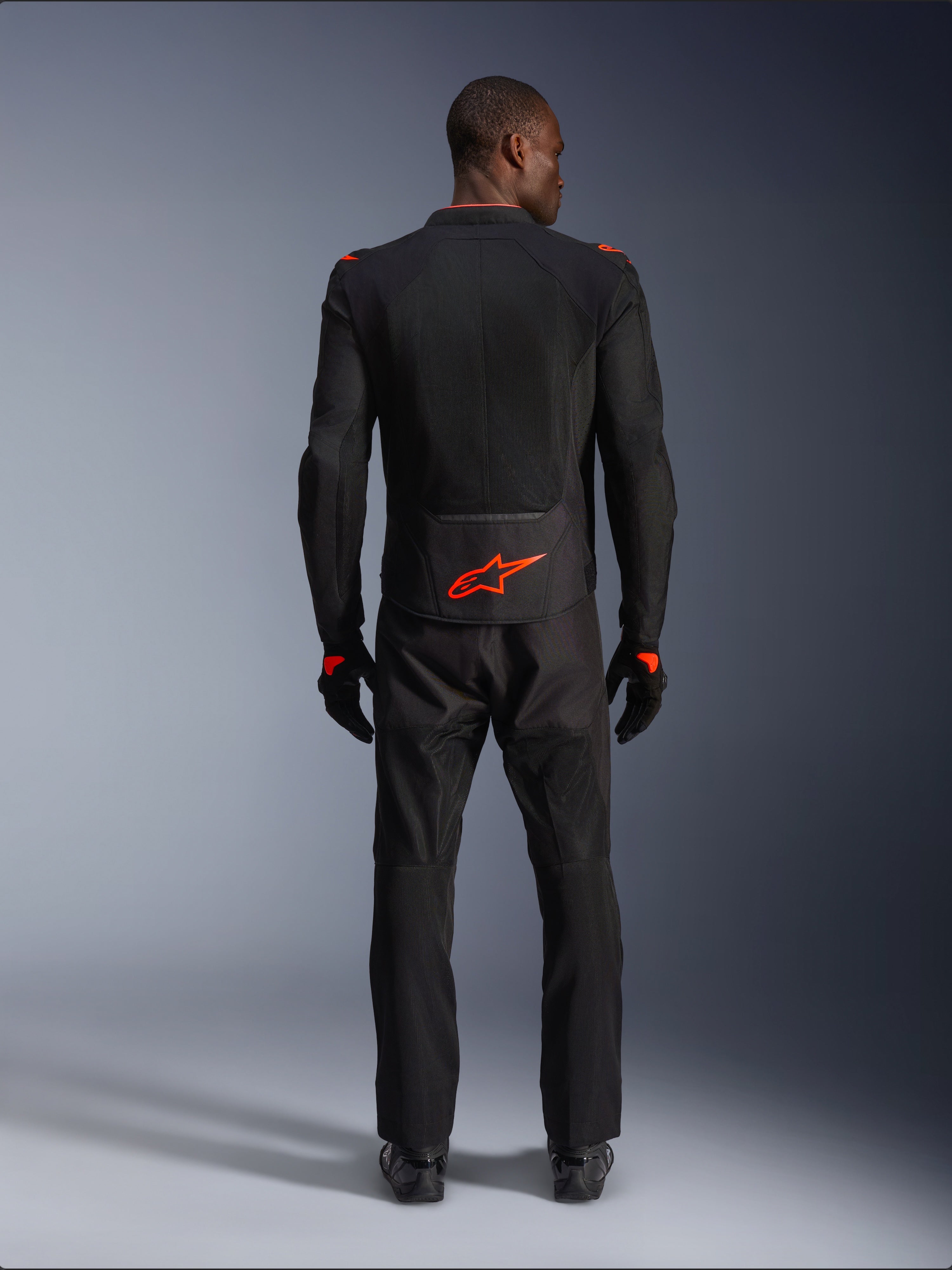 Veste Alpinestars Viper Air V4, noir et rouge fluo, vue de dos sur mannequin, portée avec un pantalon et des gants de moto assortis, logo rouge fluorescent vif au bas du dos, construction en mesh pour la circulation de l'air, coupe athlétique pour la conduite sur route