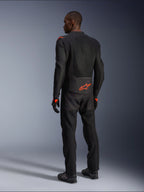 Pilote homme vu de dos portant la veste Alpinestars Viper Air V4, noir et rouge fluo, logo Astars orange sur le bas du dos et les épaules, construction en textile mesh, avec pantalon et bottes de moto noirs assortis