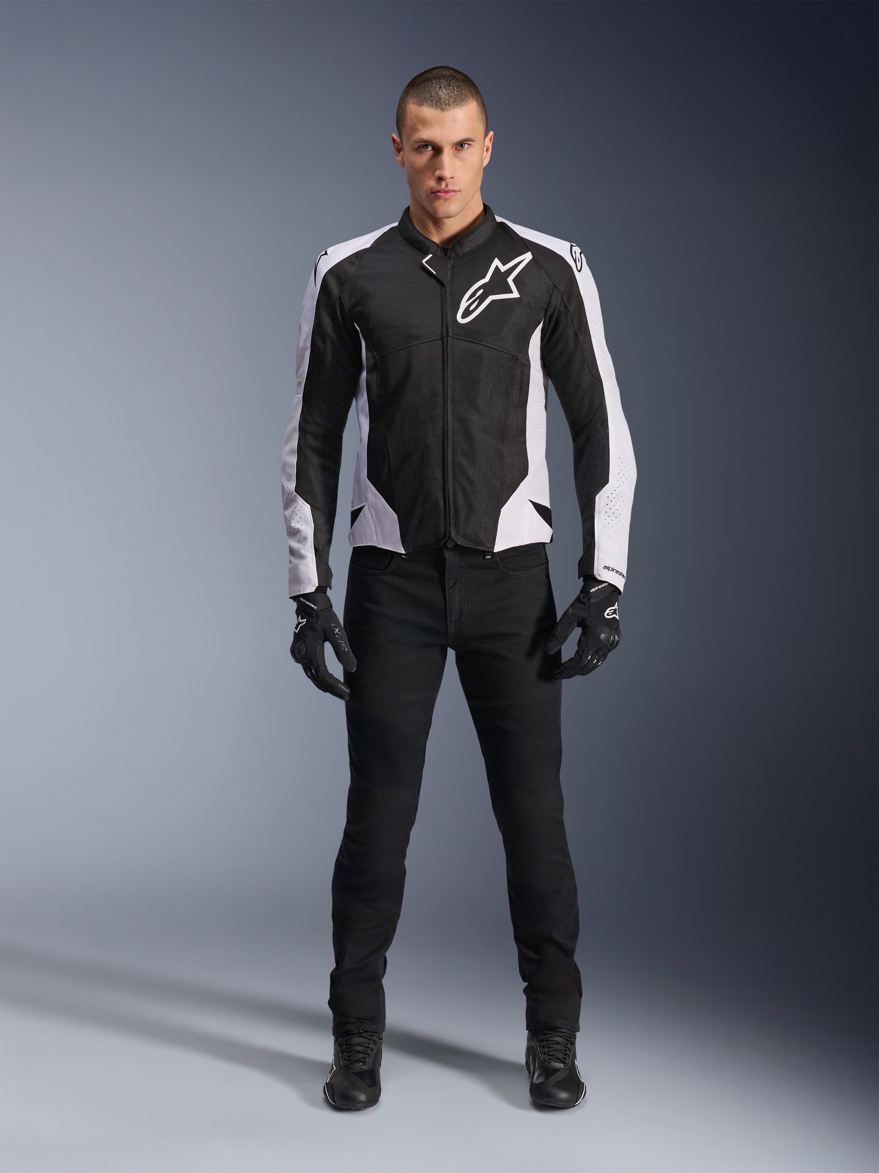 Alpinestars Viper Air V4 Jas, zwart-witte motorjas met groot wit logo op de borst, gedragen door een mannelijk model met zwarte broek en handschoenen, voorzien van meshpanelen voor ventilatie, sportieve motorkleding voor op de weg