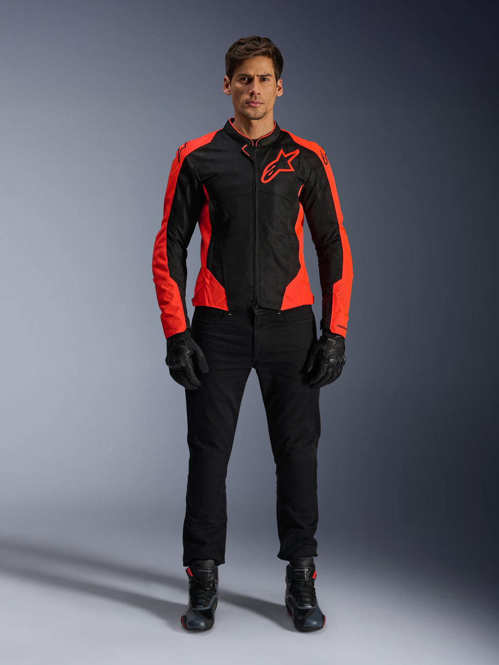 Modèle masculin portant la veste Alpinestars Viper Air V4 rouge fluo et noire, avec pantalon, gants et bottes de moto noirs, panneaux en maille respirante et logo étoile sur la poitrine, tenue de route sportive pour moto
