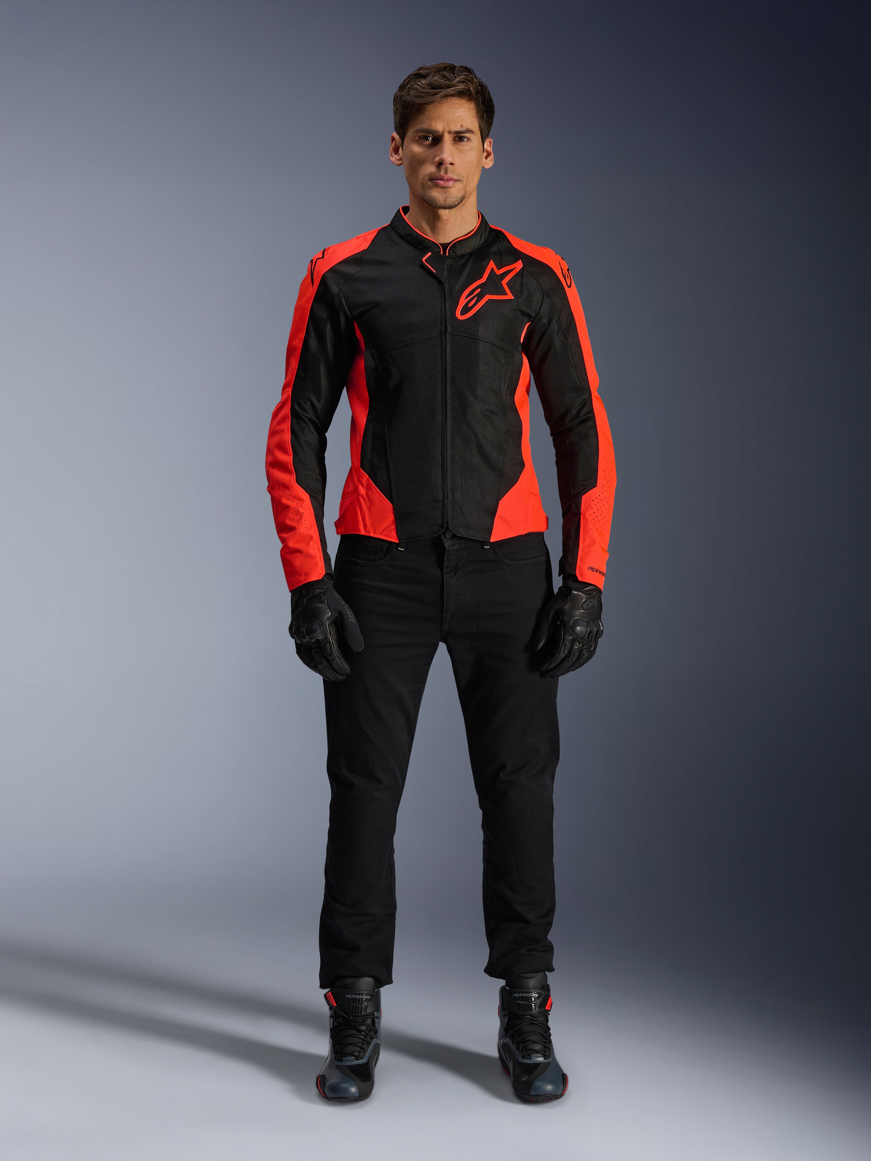 Modèle masculin portant la veste Alpinestars Viper Air V4 rouge fluo et noire, avec pantalon, gants et bottes de moto noirs, panneaux en maille respirante et logo étoile sur la poitrine, tenue de route sportive pour moto