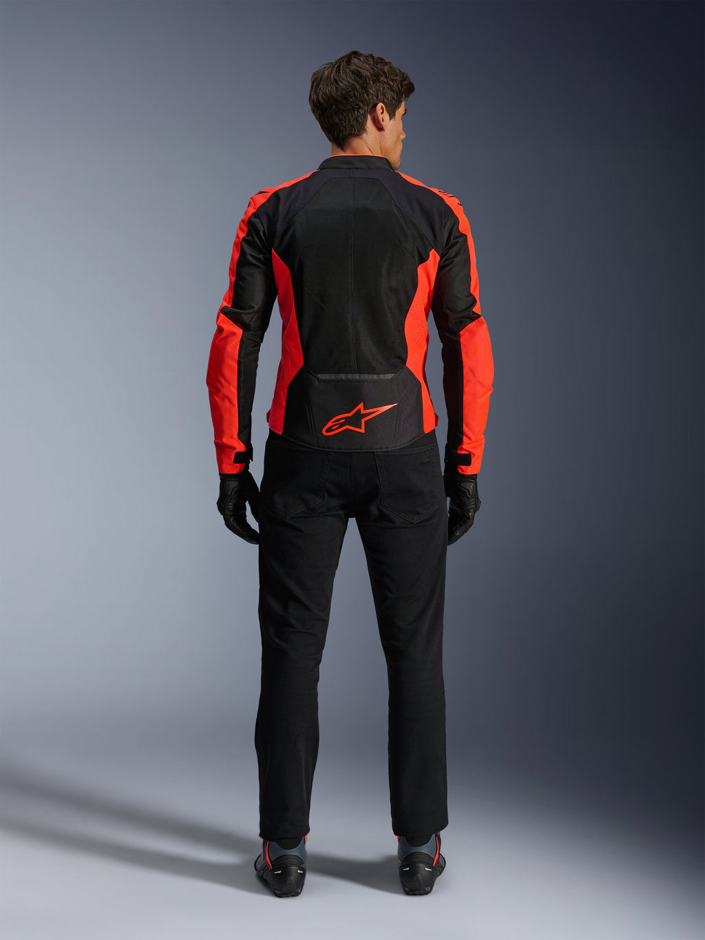 Veste Alpinestars Viper Air V4, rouge fluo et noir, vue de dos montrant de larges panneaux en maille technique et des accents latéraux rouge fluo, logo Alpinestars rouge dans le bas du dos, portée avec un pantalon de moto et des gants noirs