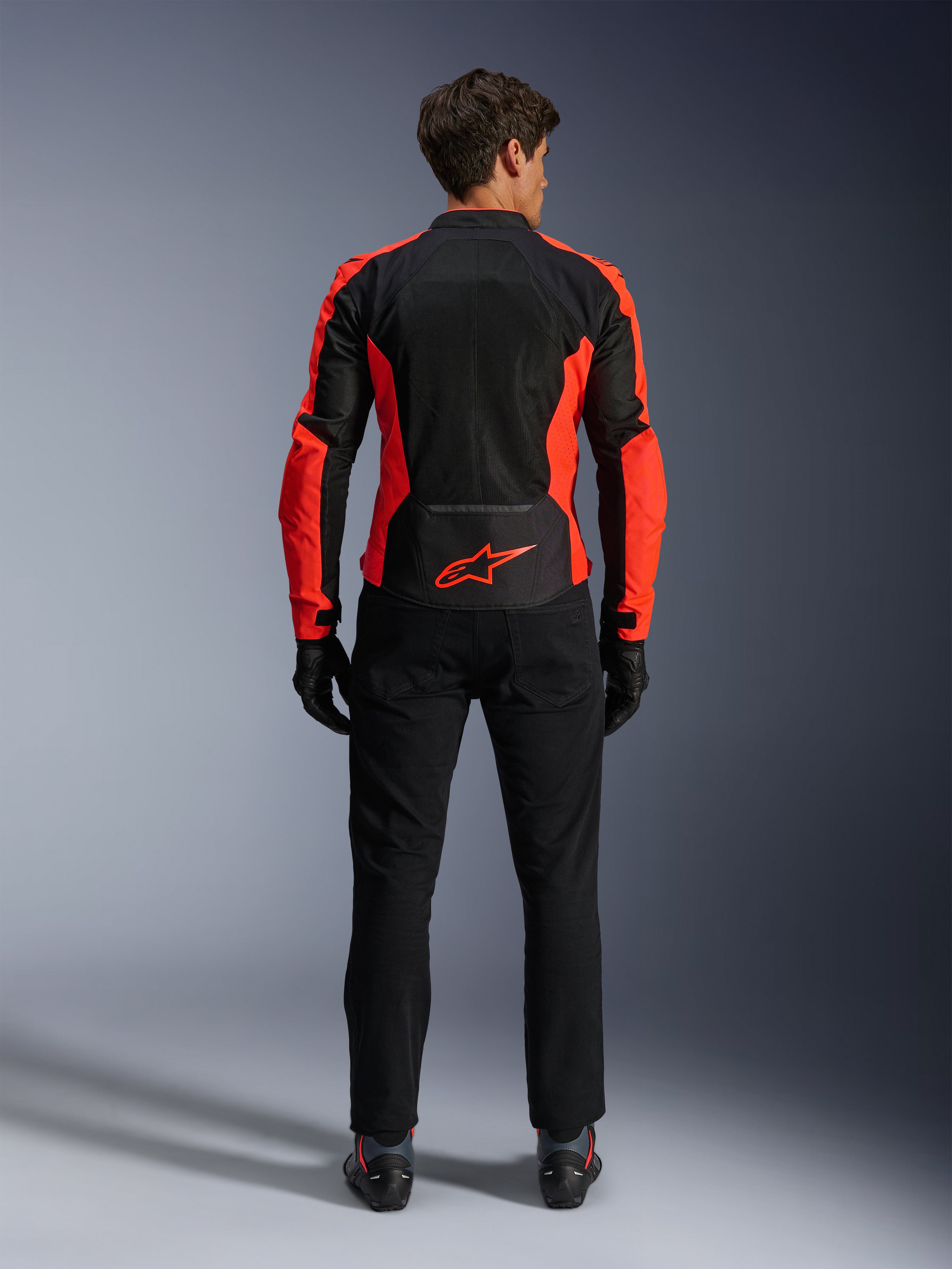 Veste Alpinestars Viper Air V4, rouge fluo et noir, vue de dos montrant de larges panneaux en maille technique et des accents latéraux rouge fluo, logo Alpinestars rouge dans le bas du dos, portée avec un pantalon de moto et des gants noirs