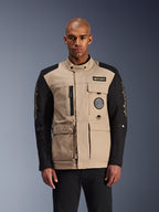 Veste Alpinestars Dice, veste de moto urbaine, beige et noire, esthétique workwear robuste avec plusieurs poches utilitaires et des écussons sur la poitrine, col haut avec fermeture à bouton, logos imposants sur les manches, portée par un mannequin homme