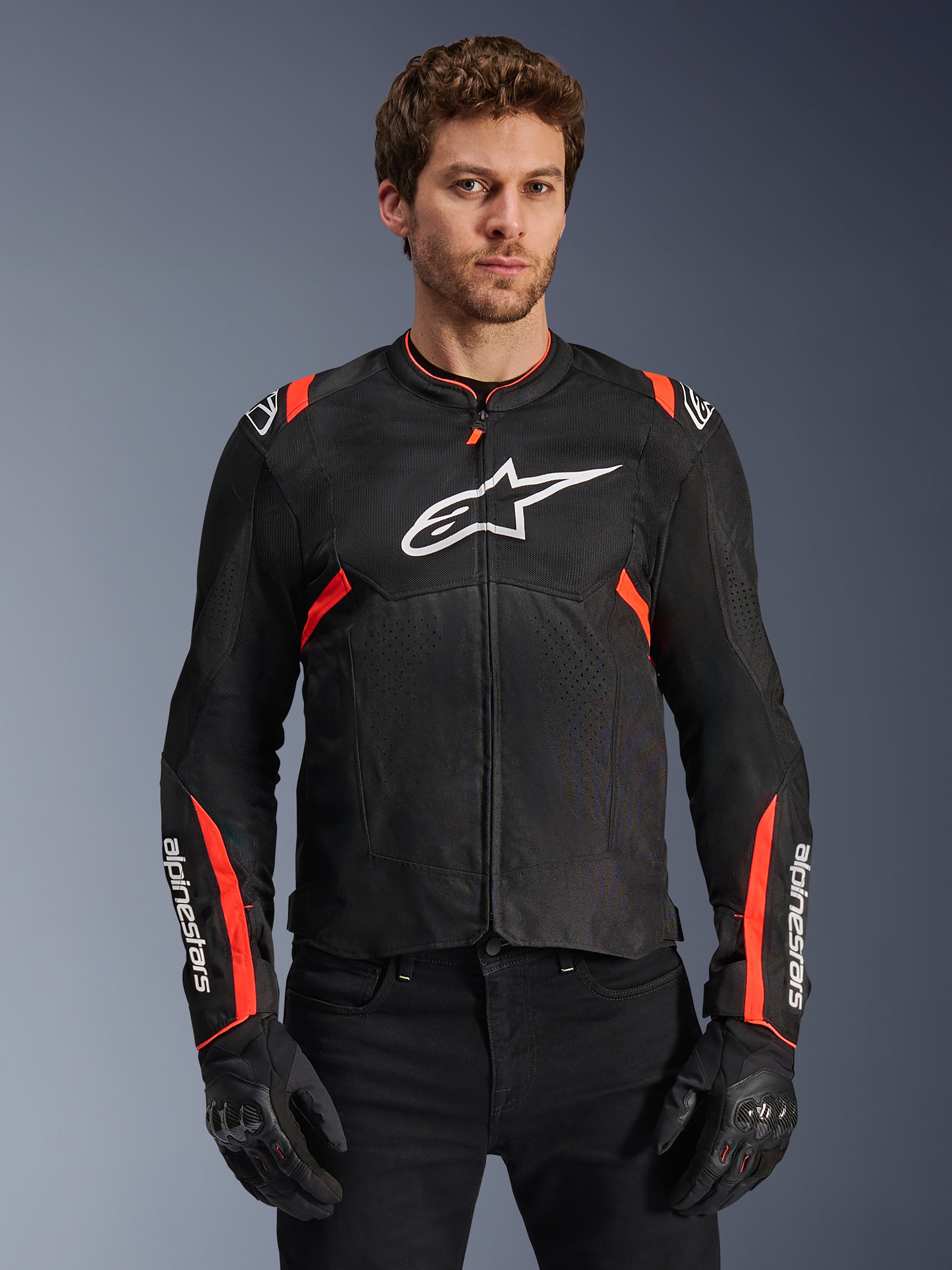 Alpinestars T-Sps Air V2 Jacke, Motorradjacke in Schwarz und Rot Fluo, großes weißes Astars-Logo auf der Brust, strukturierte Tech-Mesh-Konstruktion für Luftzirkulation, getragen von einem Model mit schwarzen Motorradhandschuhen, sportliches Design mit roten Akzenten an Schultern und Ärmeln