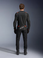 Alpinestars T-SPS Air v2 Jacke in Schwarz und Rot Fluo, Rückansicht mit großen Mesh-Belüftungseinsätzen und weißem Alpinestars-Logo auf dem unteren Rücken, getragen mit schwarzer Motorradhose und Stiefeln.