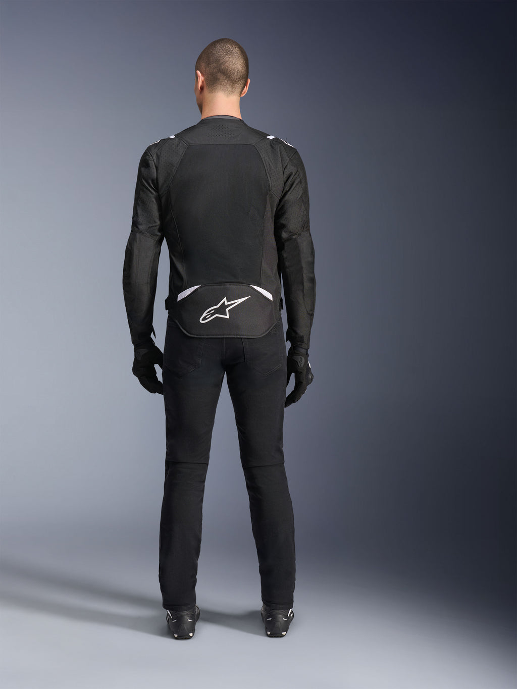 Alpinestars T-Sps Air V2 Jacke, Rückansicht, schwarz-weiße Textil-Motorradjacke, mit großem Mesh-Rückenpanel für maximale Luftzirkulation und weißem Astars-Logo am unteren Rücken, kombiniert mit schwarzer Motorradhose und Handschuhen