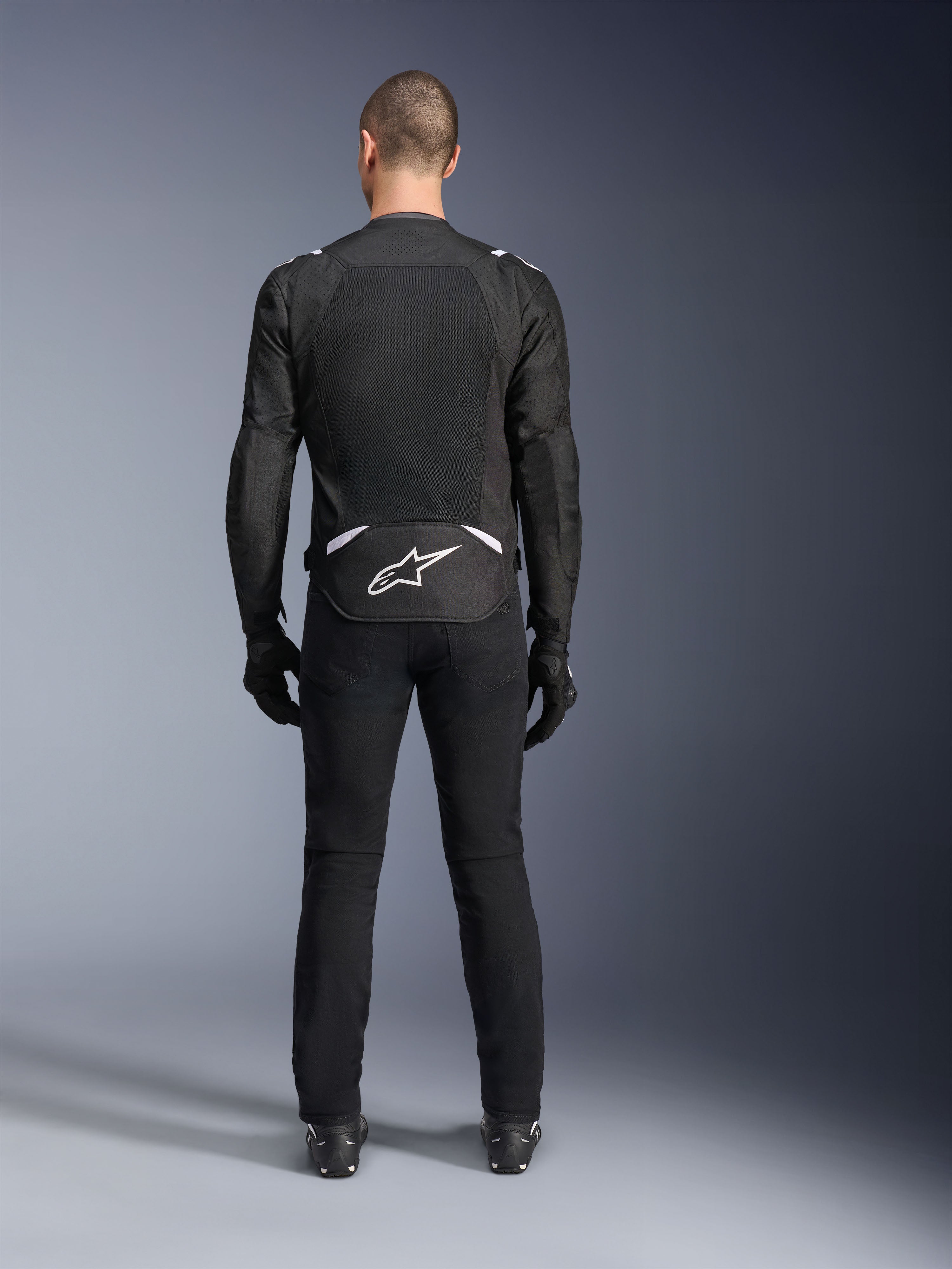 Alpinestars T-Sps Air V2 Jacke, Rückansicht, schwarz-weiße Textil-Motorradjacke, mit großem Mesh-Rückenpanel für maximale Luftzirkulation und weißem Astars-Logo am unteren Rücken, kombiniert mit schwarzer Motorradhose und Handschuhen