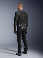 Alpinestars T-Sps Air V2 Jacke, Textil-Motorradjacke, Schwarz, Rückansicht mit großem Mesh-Belüftungspanel und weißem Alpinestars-Logo am unteren Rücken, kombiniert mit schwarzer Motorradhose und Handschuhen für einen sportlichen urbanen Look.