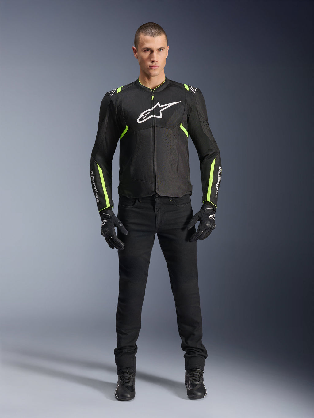 Alpinestars T-Sps Air V2 Jacke, Schwarz und Gelb Fluo, Textil-Motorradjacke mit Mesh-Einsätzen, getragen von einem männlichen Model mit schwarzer Hose und Handschuhen, weißes Alpinestars-Logo auf der Brust, urbane Sport-Motorradausrüstung