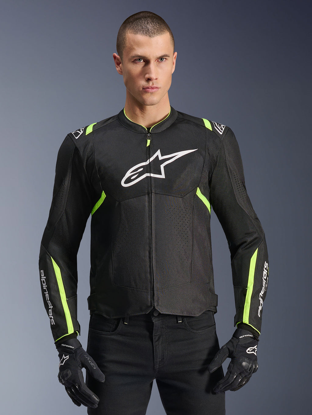 Alpinestars T-Sps Air V2 Jacke in Schwarz Gelb Fluo, männliches Modell in belüfteter Textiljacke mit Mesh-Einsätzen und weißem Brustlogo, kombiniert mit schwarzen Motorradhandschuhen, urbane Motorradausrüstung