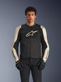 Veste Alpinestars T-SPS Air V2, veste de moto, noir et mastic aluminium, modèle masculin portant la veste avec un pantalon et des gants noirs, avec panneaux en maille pour la ventilation, grand logo Alpinestars sur la poitrine et design sportif ajusté