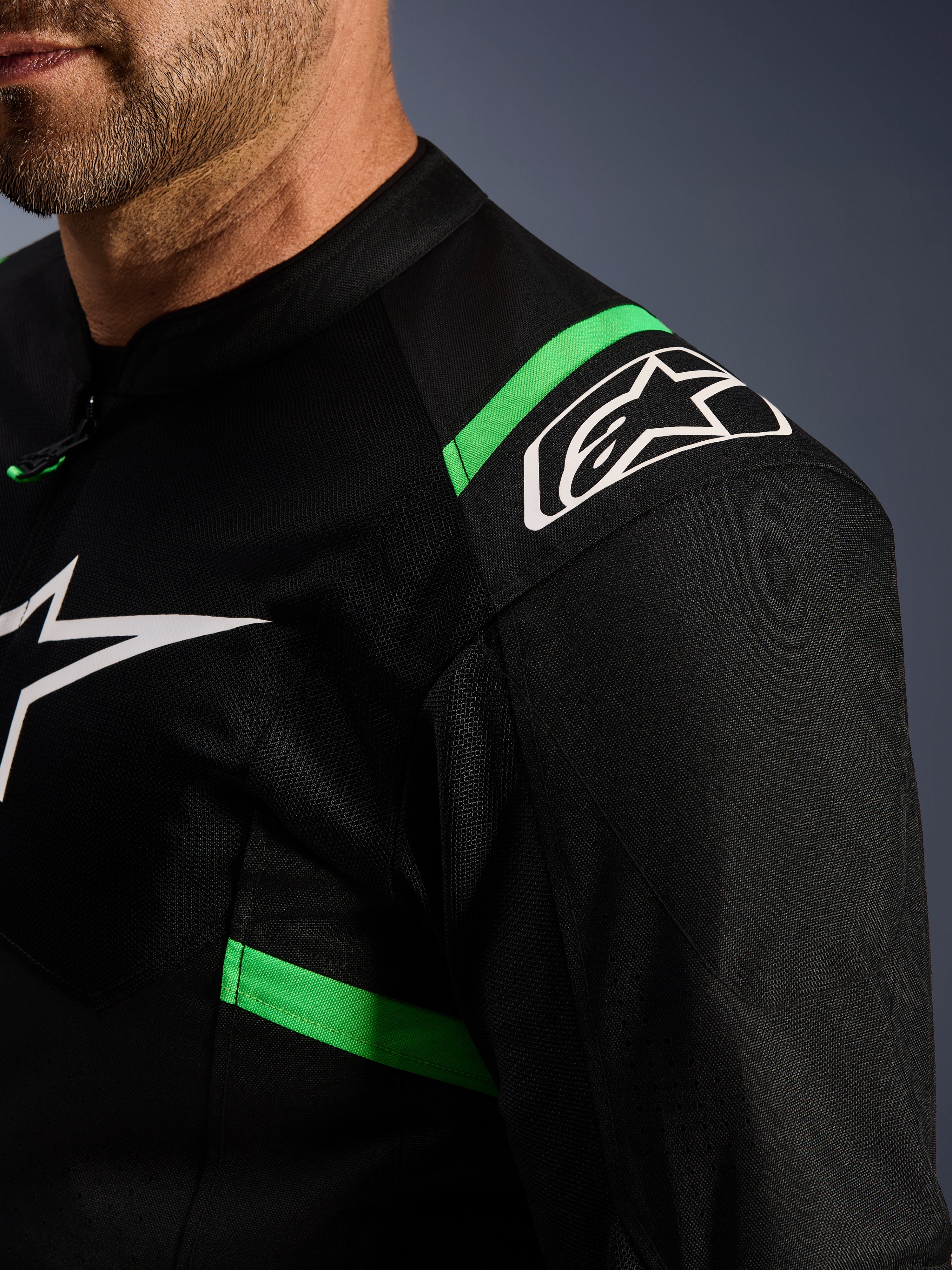 Alpinestars T-SPS Air V2 Jacke, Schwarz und Fluo-Grün, Nahaufnahme des Schulter- und Brustbereichs, weißes Alpinestars Stern-Logo, technisches Mesh-Gewebe für Belüftung, sportliche Motorradjacke