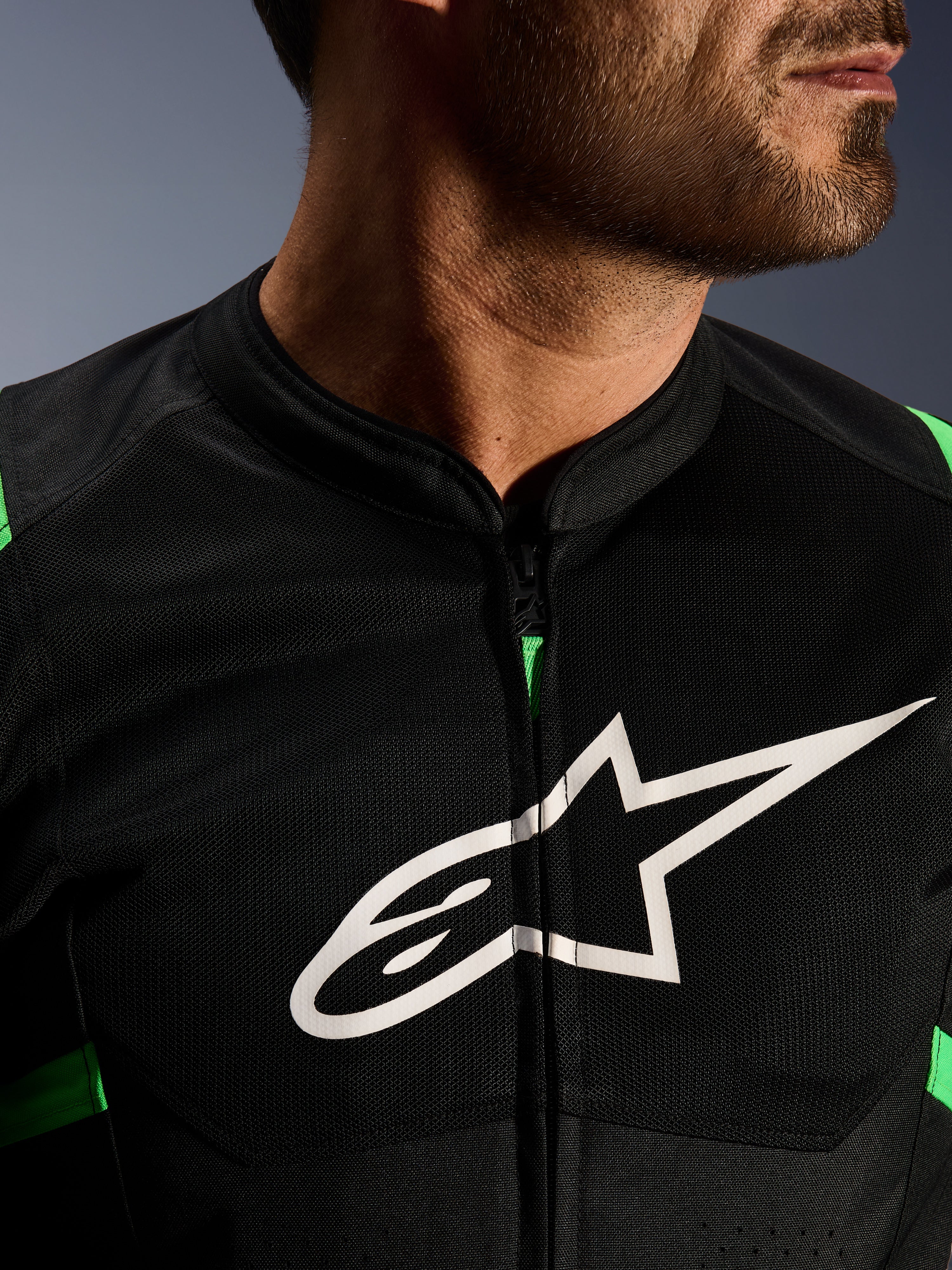 Nahaufnahme der Alpinestars T-SPS Air V2 Jacke, Schwarz und Neongrün, mit atmungsaktiven Tech-Mesh-Einsätzen, zentralem Reißverschluss und markantem weißen Alpinestars-Sternlogo auf der Brust, Performance-Motorradausrüstung