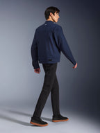 Alpinestars Bruiser Jacket en Bleu Foncé, veste de moto urbaine en textile, vue arrière d'un mannequin qui marche, associée à un pantalon noir et des baskets à semelles en gomme, dotée d'un design inspiré du style workwear et de pattes de réglage à la taille.